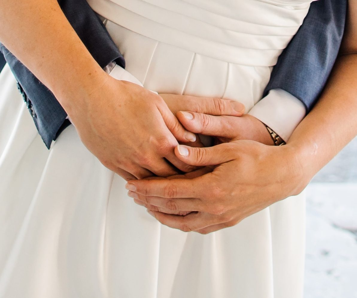 Händchen haltende Paare um den Bauch einer Braut in einem eleganten Kleid.