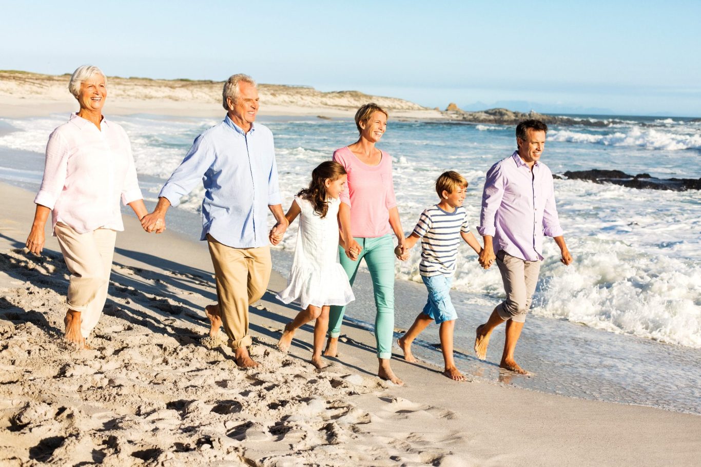 Familie geht Hand in Hand am Strand entlang, Wellen schlagen sanft am Ufer.